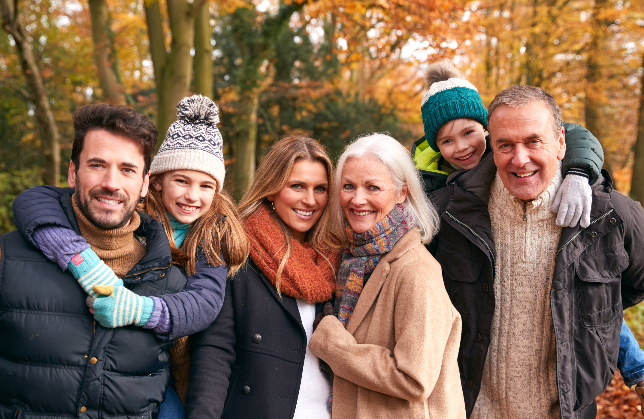 Portrait Of Smiling Multi Generation Family Walking Along Autumn Woodland Path